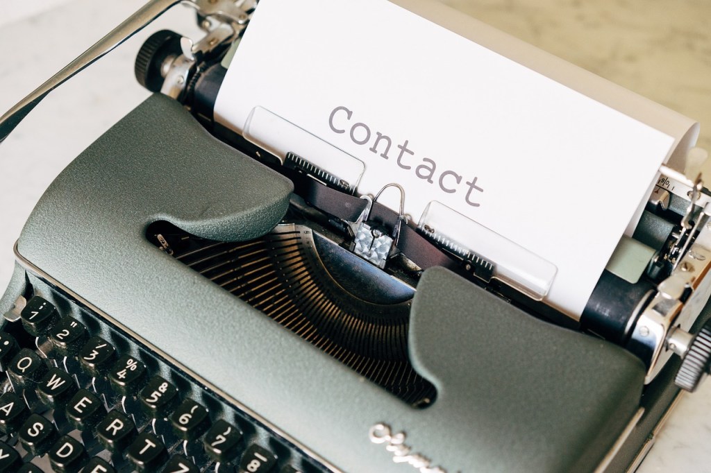 A picture of an old typewriter with a piece of paper in it that has had the word 'contact' typed upon it.